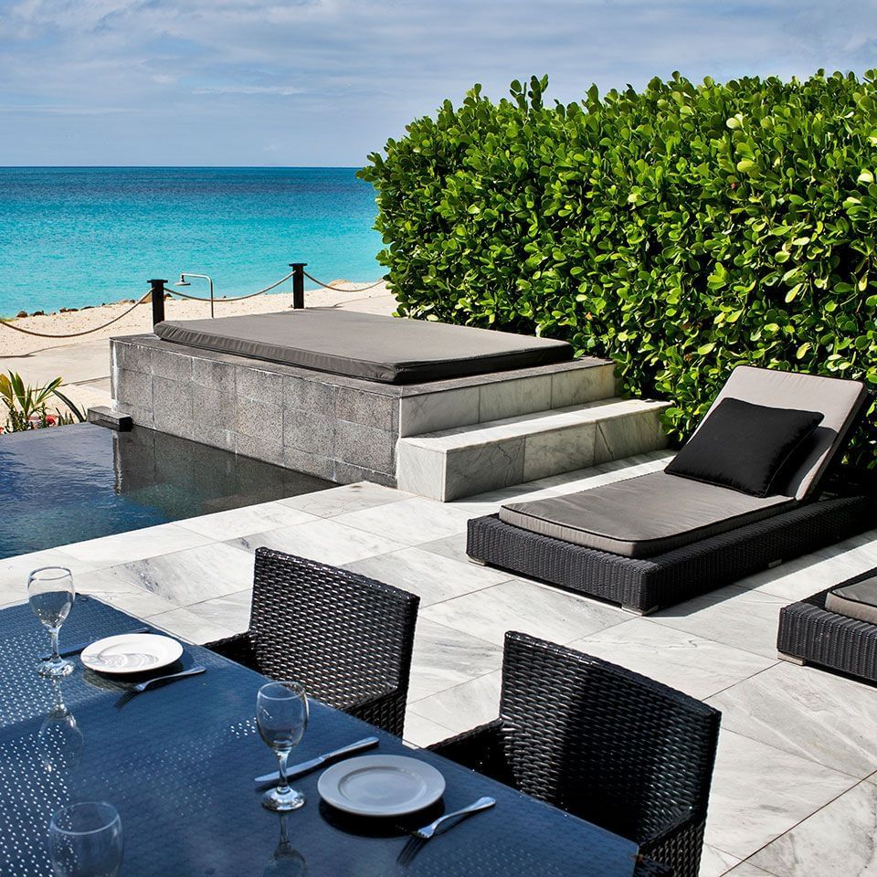  Outdoor patio with dining table, lounge chairs, and a daybed overlooking the ocean and lush foliage.
