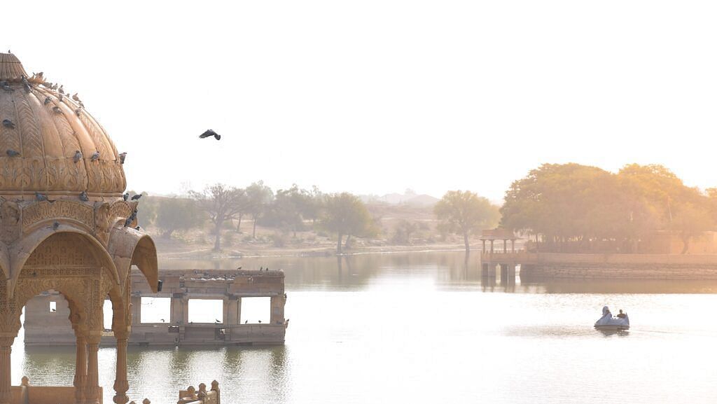 An image of a lake with a palace structure in the foreground and lush greenery in the background