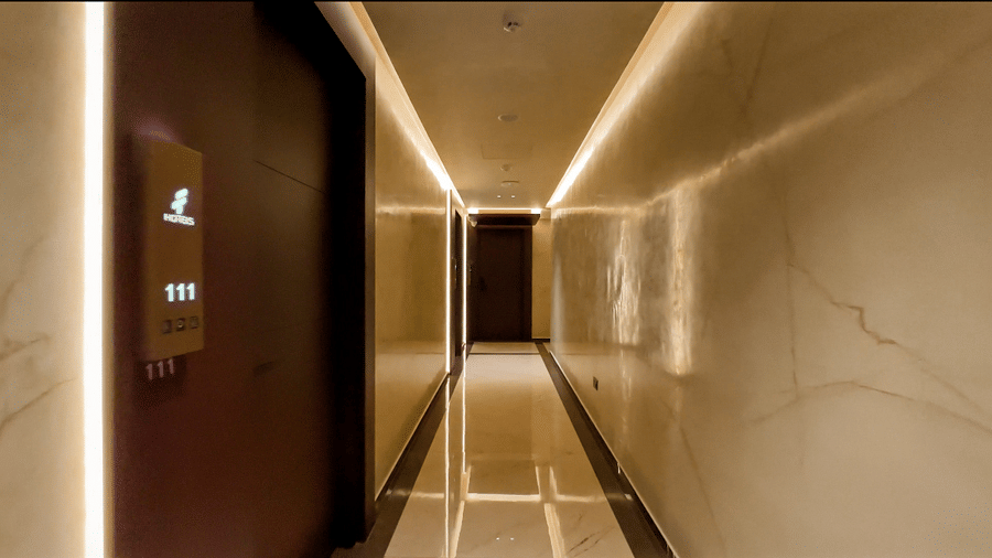 A brightly lit corridor at F Hotels, Bengaluru, featuring a wooden door of a room in the starting.