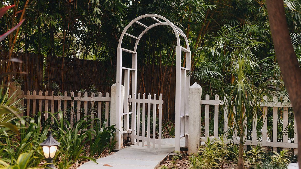 A facade image of the Lions Den Karma Chalets featuring an entry gate with lush greenery.