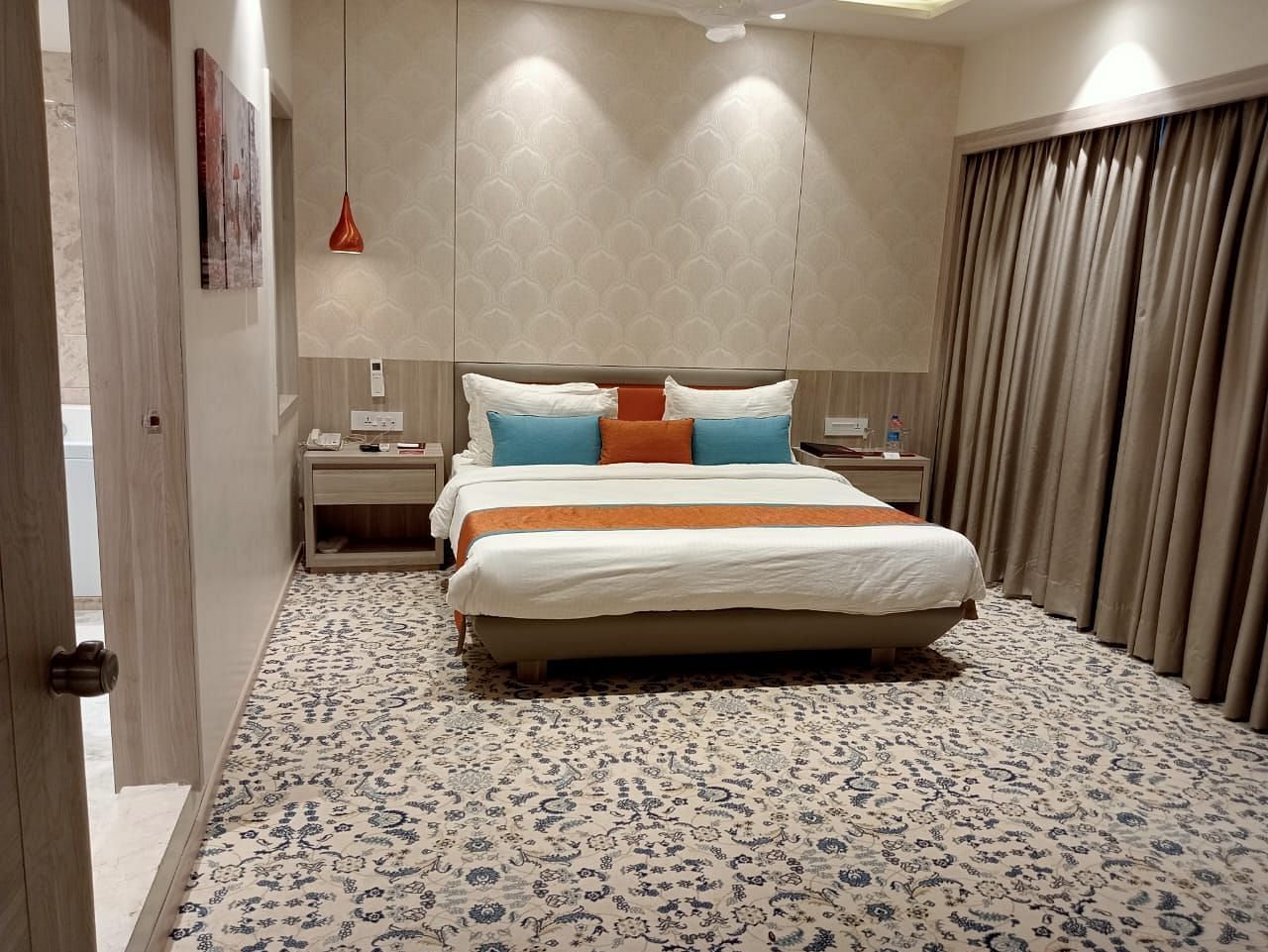 A contemporary hotel bedroom featuring a large bed with white bedding, decorative cushions, and warm ambient lighting.