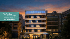 Web banner of Tulip Inn Gurugram featuring the facade of the hotel with illuminated signage under a dark cloudy sky, with a box on one side saying the property is 'Now Open'.