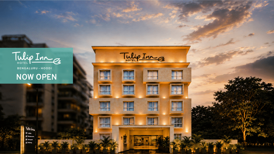Website banner of Tulip Inn, Hoodi Whitefield, Bengaluru, showcasing the property facade, with the signage reading 'Tulip Inn', a 'Now Open' block, and a partially cloudy sky in the background.