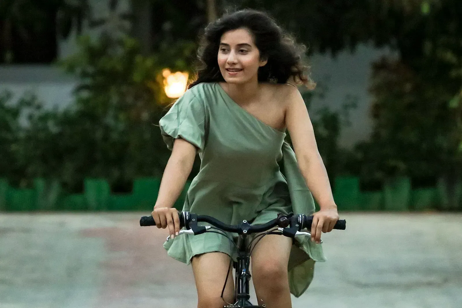 A woman cycling on a pathway with a blurred background of plants and a light at Daksh Eden Greenz, Sasan Gir.