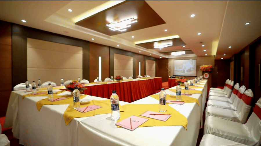 A professional conference hall at S Hotels, Chennai with a projector screen, modern recessed lighting, and individual water bottles set for a corporate event.