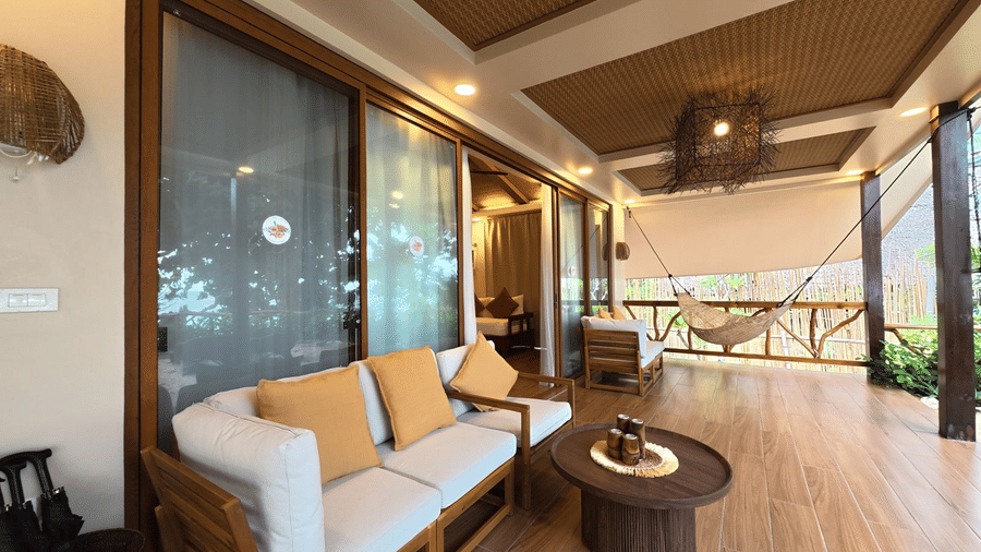 A seating area with a sofa, pillows, a table, and fence. | Flower Island Resort