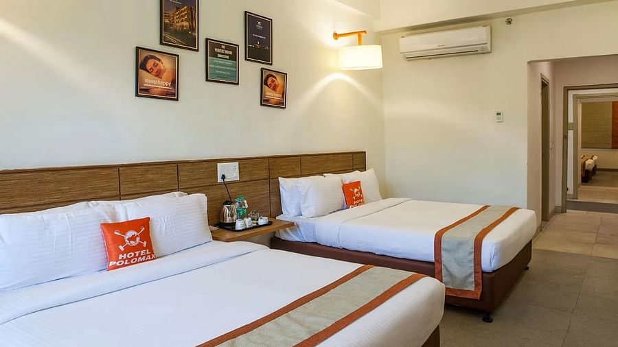 full view image of the max family room featuring two plush double beds along with a split air-conditioner and a bedside table between the two beds - Max Hotel Jabalpur