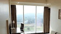 A well-lit area with a comfortable couch facing a glass window. A TV is mounted nearby, creating a relaxing ambiance.- Golden Suites, Gurgaon