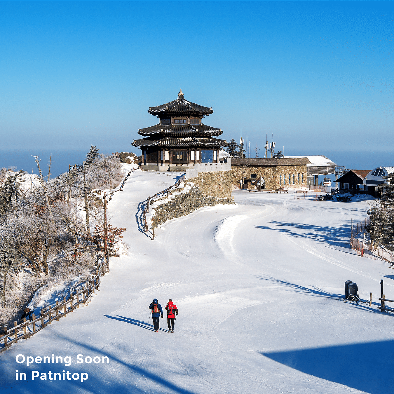 Mountain top coated with snow as two people walk to the temple at the crest under the clear blue sky as the text on the image says 'Coming Soon in Patnitop'