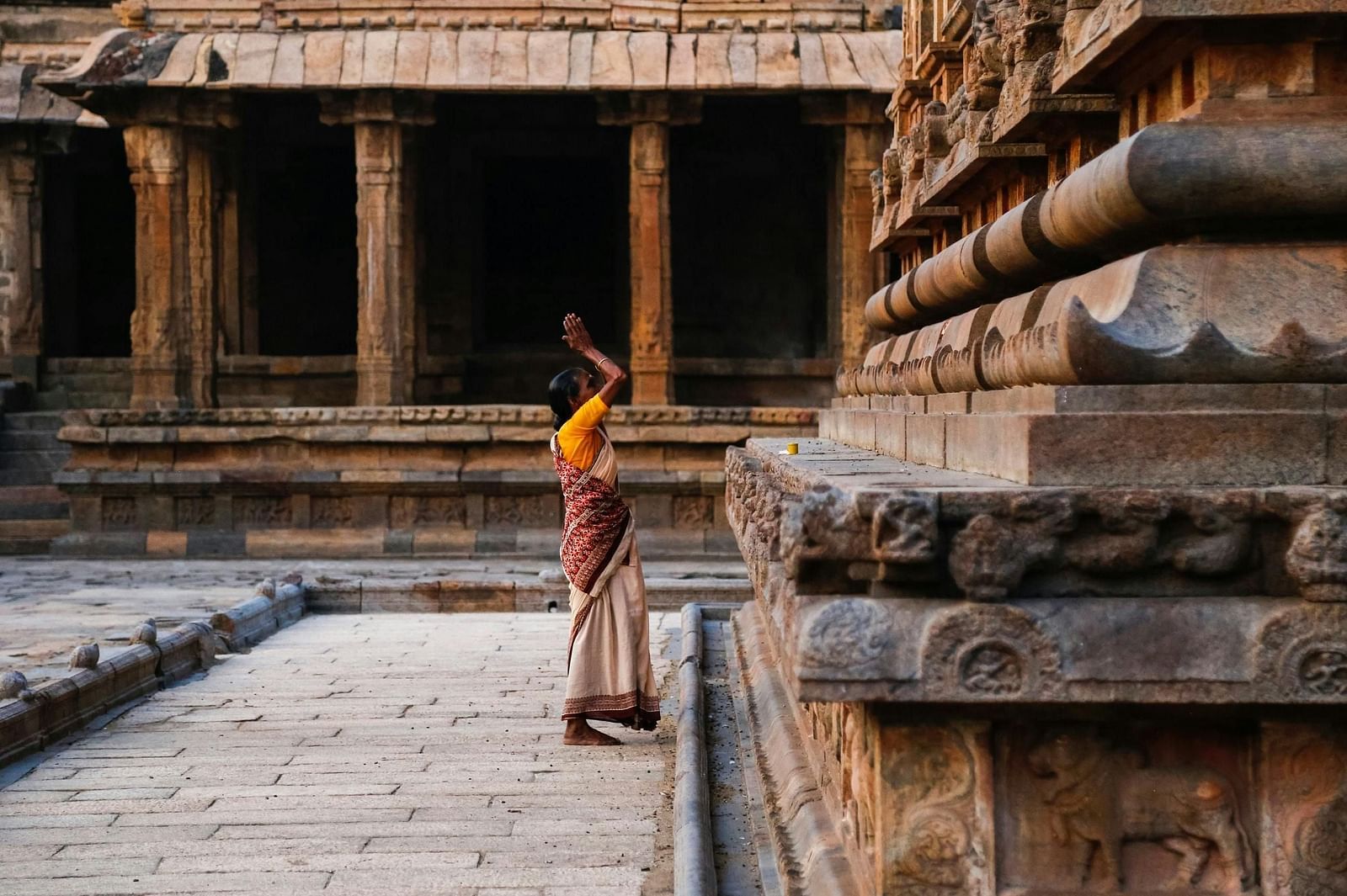 A woman in a saree praying to god inside a temple complex.