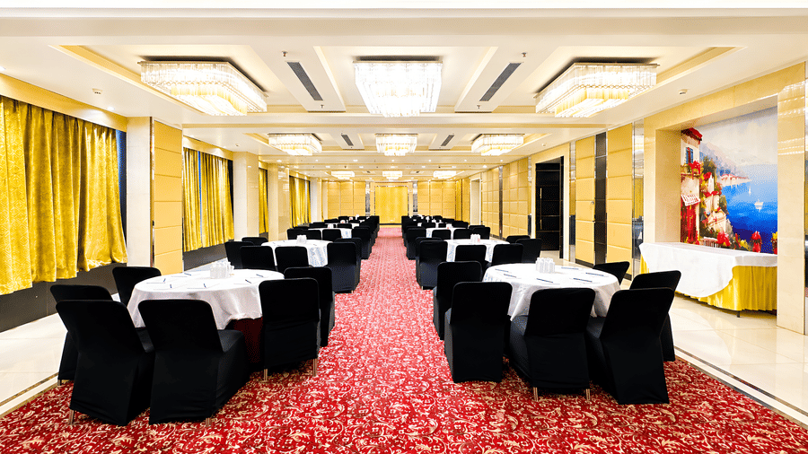 Reception area at Golden Tulip Kukas Jaipur featuring a white front desk, ornate dark patterned wall, marble floors, and warm overhead lighting.