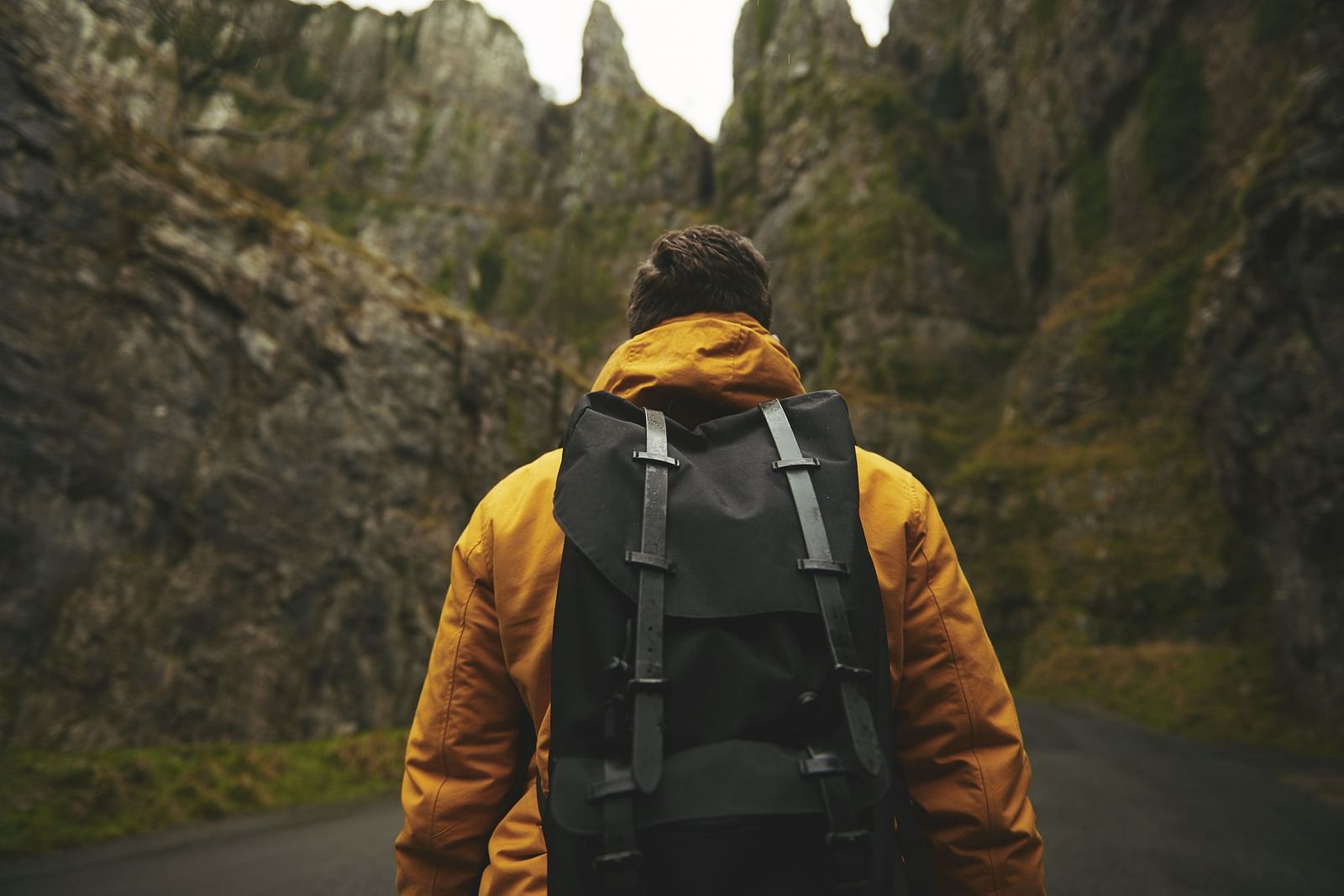 A close up shot of a person walking towards a mountain range while wearing a backpack.