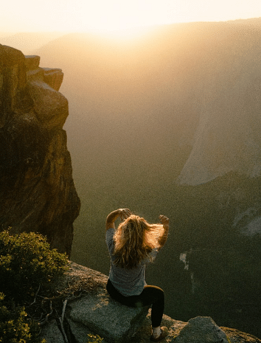 A woman sitting on a rock overlooking a valley at sunset