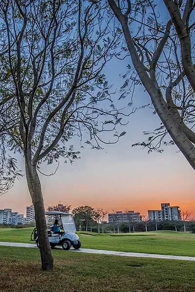 Person sitting under trees near a golf course at sunset with buildings in the background at Karma Chalets.