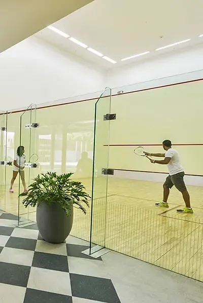 Two people playing squash on an indoor court with glass walls at Karma Chalets.