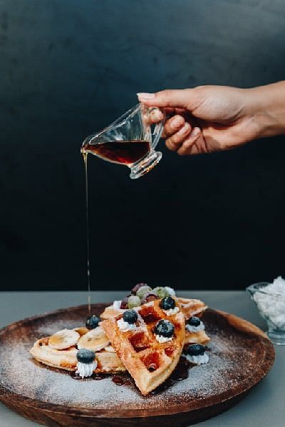 Hand pouring syrup over waffles topped with berries on a wooden plate at Karma Chalets.