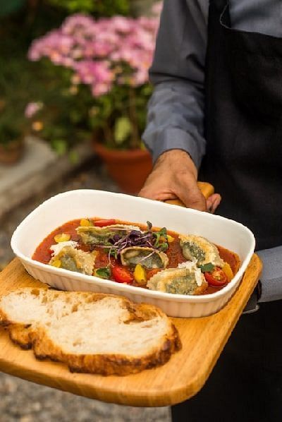 Staff member at Karma Chalets holding a wooden tray with a dish of stir-fried vegetables and two slices of bread.
