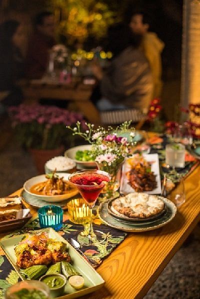 Table at Karma Chalets with a variety of plated dishes including salad, grilled meats, and desserts in a low-lit dining setup.