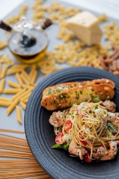 Pasta dish with grilled bread and cheese on a grey plate placed on a wooden surface at Karma Chalets.