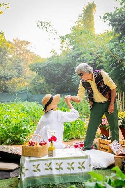 Staff member serving food to a seated guest in the garden area of Karma Chalets during daylight.