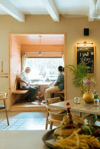Indoor dining table at Karma Chalets with food and drinks set up, and a person seated near a sunlit window.