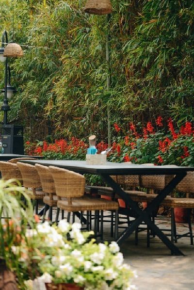 Outdoor café-style seating area at Karma Chalets with wooden tables and green chairs surrounded by plants and flowers.