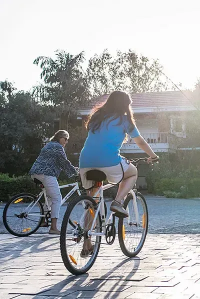 A woman and a child riding bicycles on a sunlit pavement at Karma Chalets.
