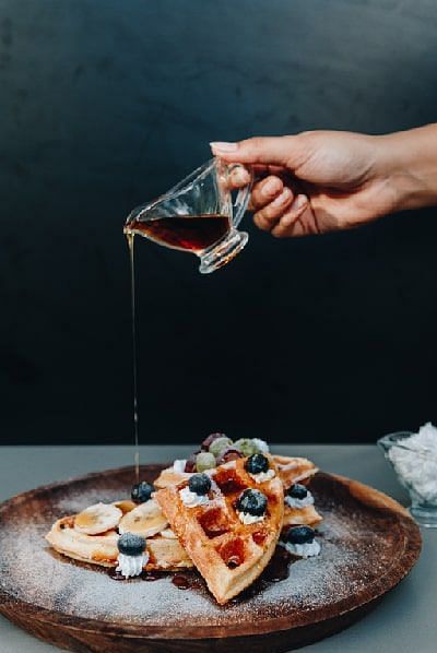 Hand pouring syrup over waffles topped with berries on a wooden plate at Karma Chalets.