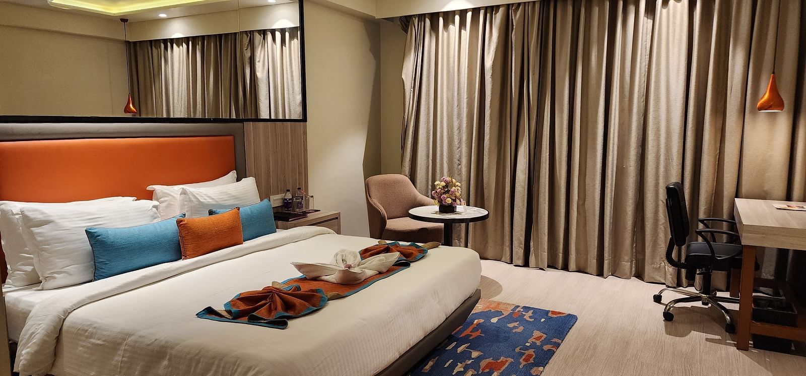 Hotel bedroom featuring rich wood finishes, floor-to-ceiling curtains, and a cosy desk area beside the bed.