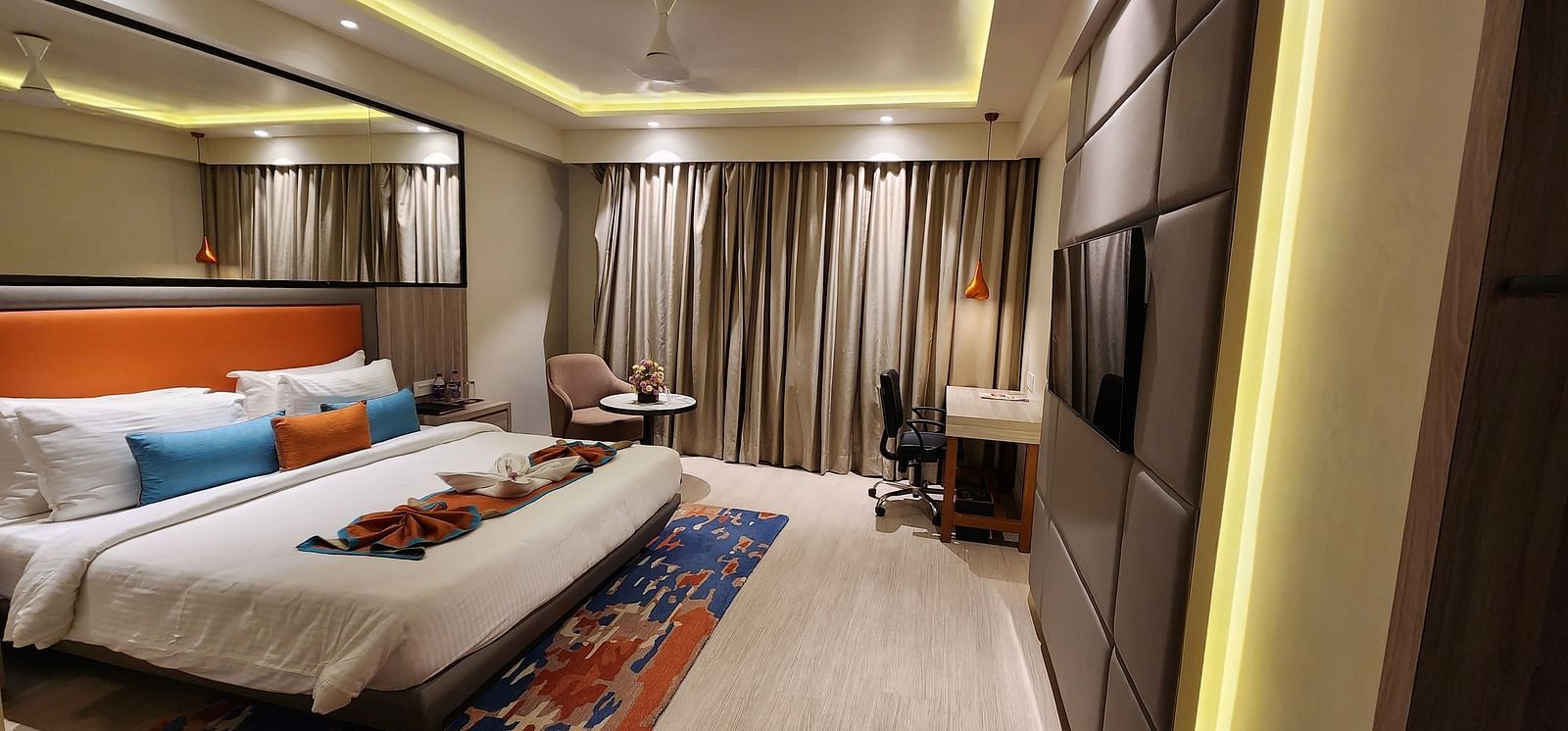 Elegant bedroom with full-length curtains, bedside tables, and a bed adorned with blue and orange cushions.