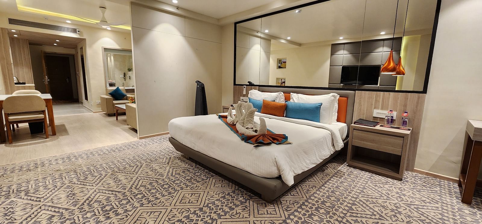 Luxurious bedroom with a king-sized bed, reading lamps, and wall-length mirror in a calm setting.