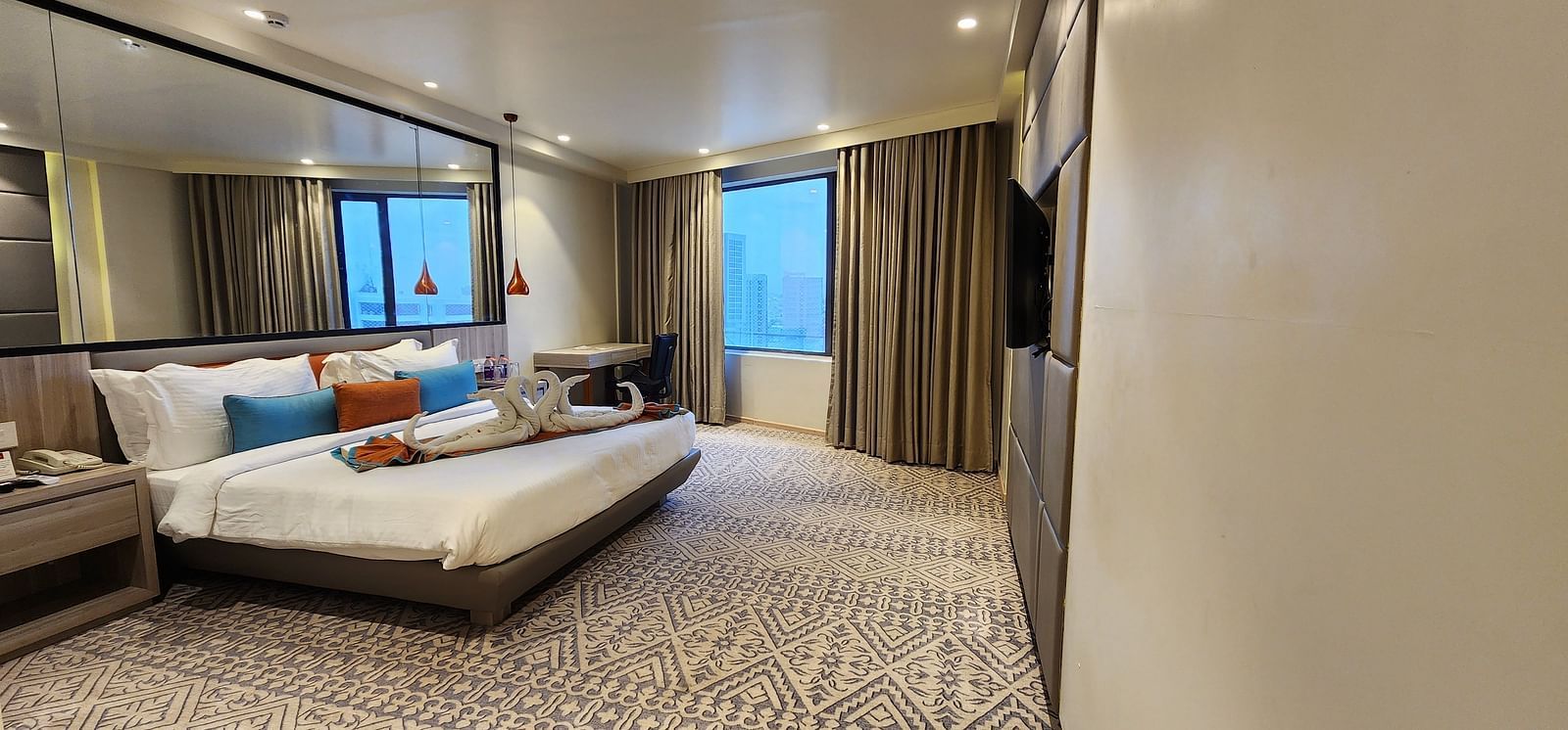 Spacious hotel suite with a modern double bed, mirrored wardrobe, and large window with curtains.