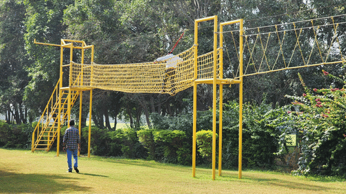 An overview of the obstacle course where a man is crossing it and a man is standing below and watching - Karma Lakelands.