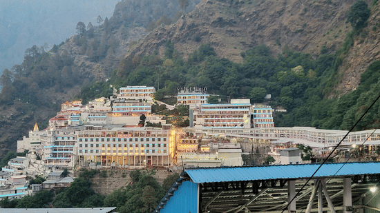 The sprawling white structures of a mountain-side shrine under a clear sky at Ananta Express, Katra.