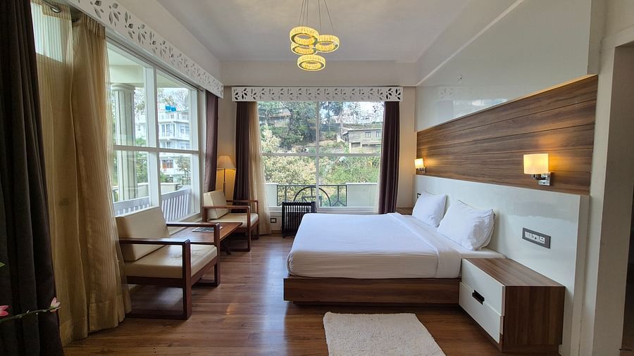 A bedroom with a white bed, a desk, and large windows, interior setting - Clarks Exotica Resort, Near Mukhteshwar.