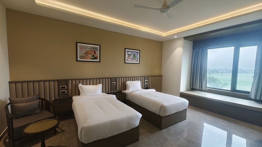 A bright room at Pride Resort, Jodhpur, featuring two single beds, seating area, and large windows with a view outside.