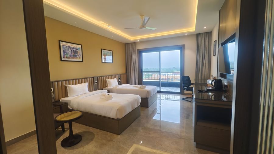 A bright and spacious hotel room at Pride Resort, Jodhpur, with two beds, seating, and large windows offering a scenic view.