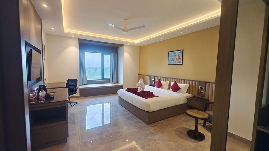 A spacious hotel room at Pride Resort, Jodhpur, featuring a large bed, desk, TV, and a window seat with a scenic view.