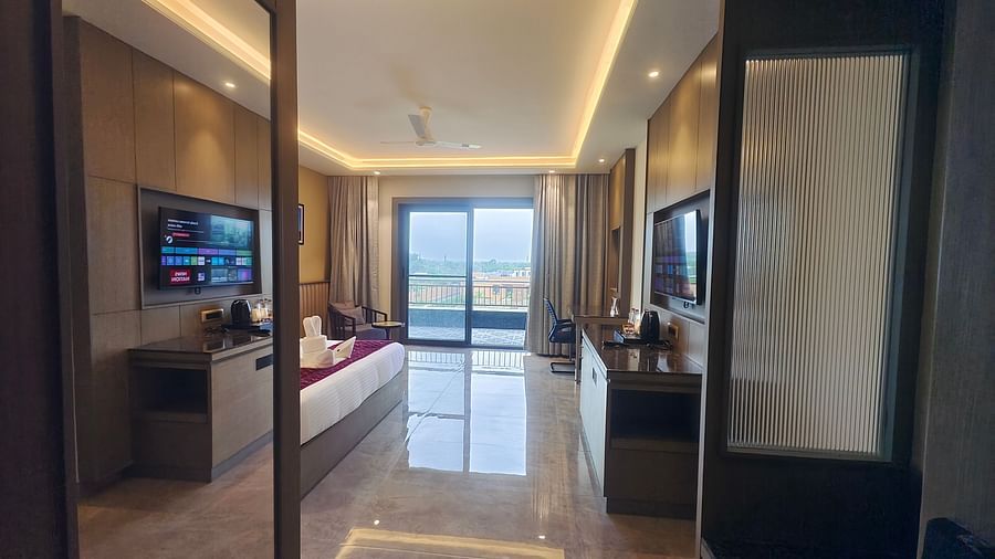 A bright hotel room at Pride Resort, Jodhpur, with a seating area, large windows, and a TV mounted on the wall.