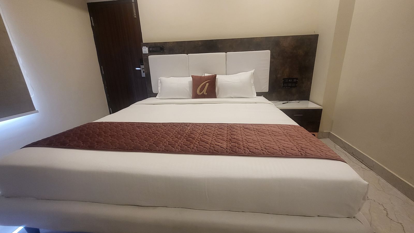 A simple and modern hotel room featuring a comfortable double bed with white linens and a decorative brown cushion - Astra Hotels and Suites, HSR Sector 7