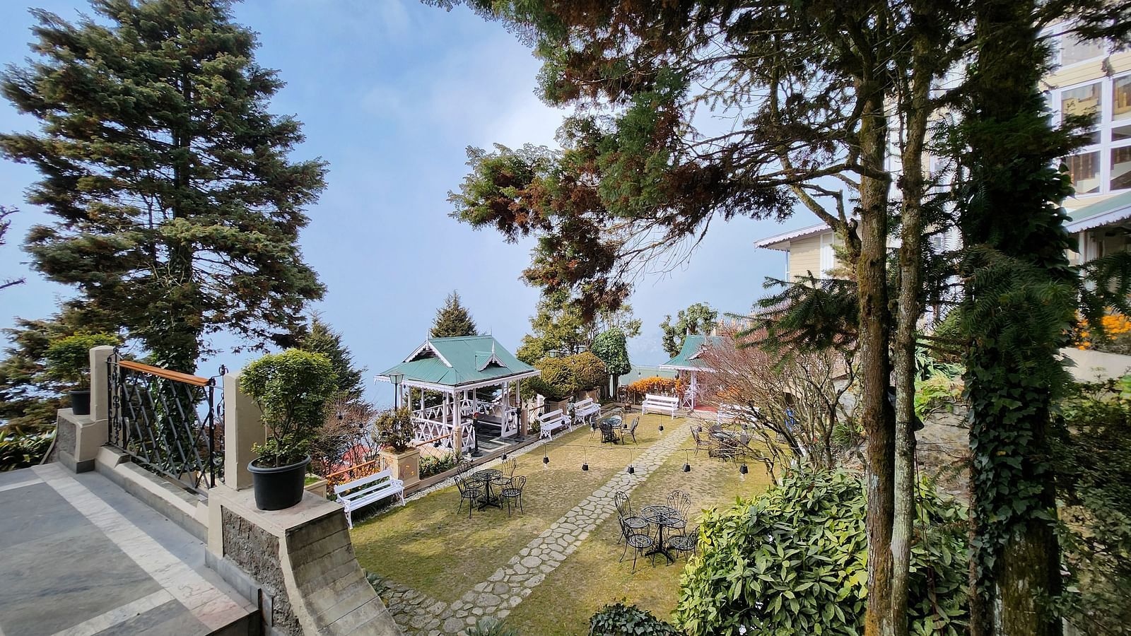 Landscaped gardens and open seating areas at Cedar Inn, Darjeeling, featuring green trees in the surrounding.