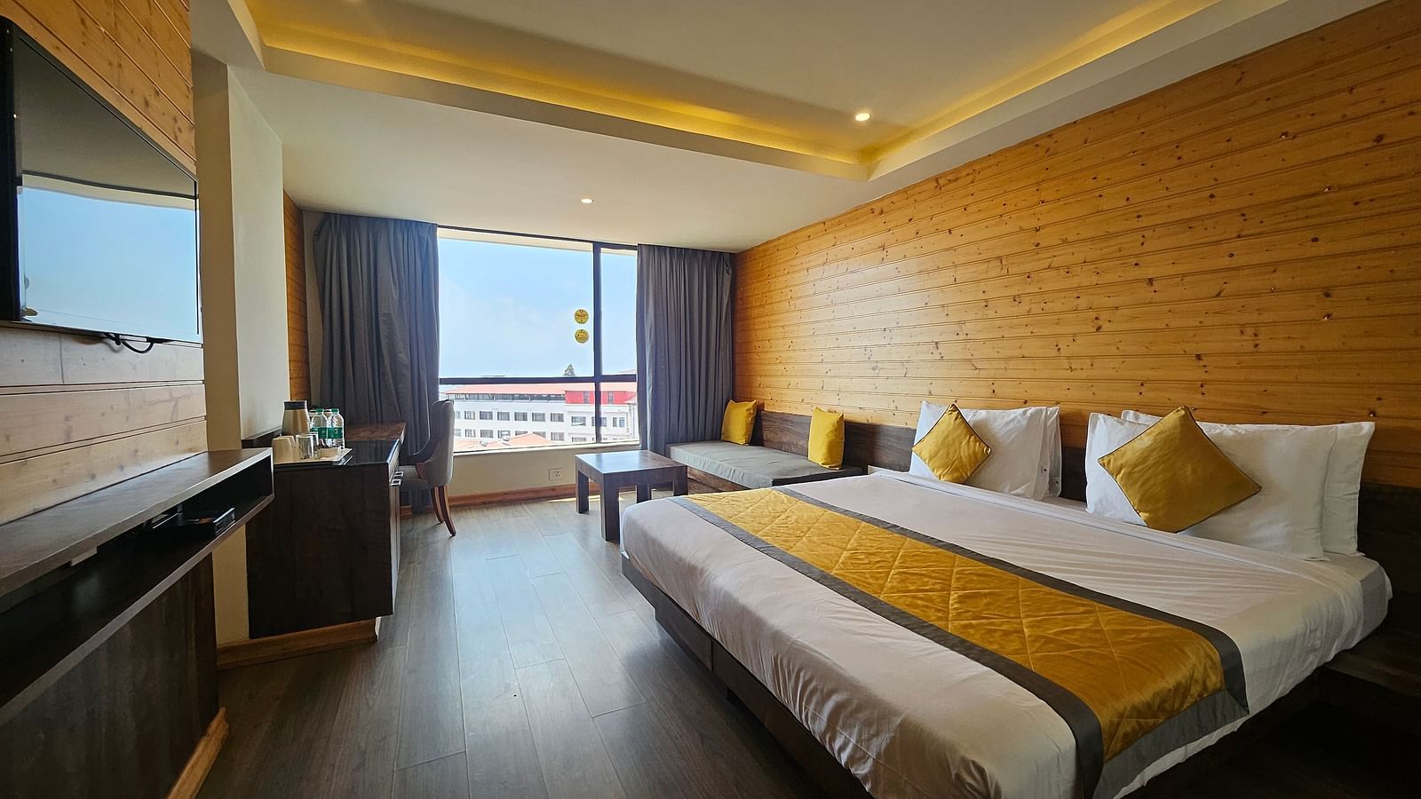 An image of a room featuring a bed, flat screen TV, basic room amenities, and an expansive window overlooking the view - Yashshree Sanderling, Darjeeling