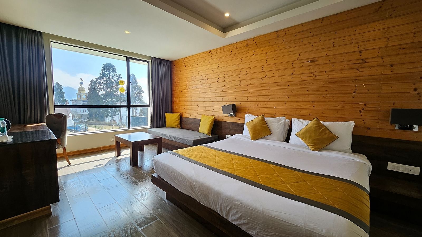 An image of a deluxe room with a bed, a couch, a table, work desk, chair, and an expansive window overlooking the view - Yashshree Sanderling, Darjeeling