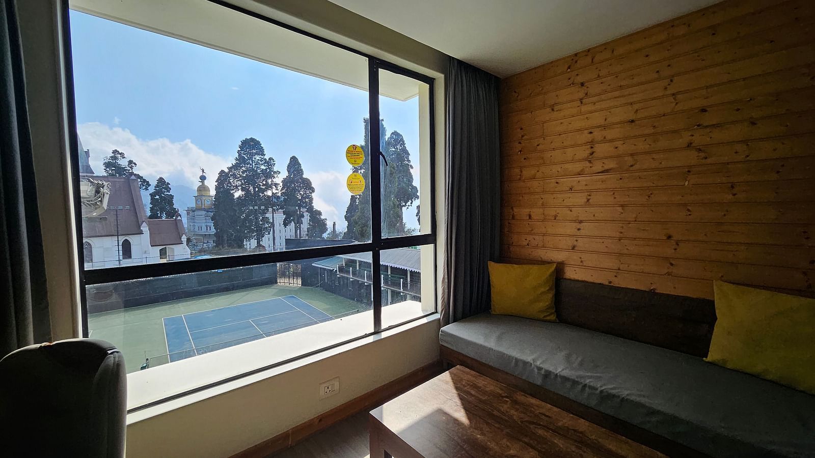 An image of a deluxe room with a couch, table, and a window overlooking the view outside - Yashshree Sanderling, Darjeeling