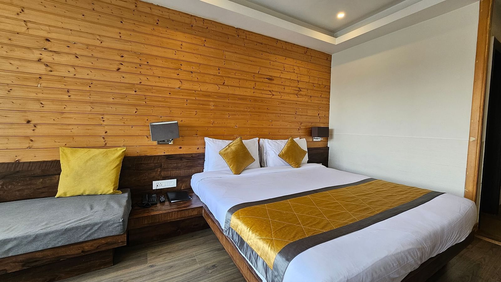 An image of a deluxe room showcasing a bed, a couch and a wooden accent wall behind the bed - Yashshree Sanderling, Darjeeling