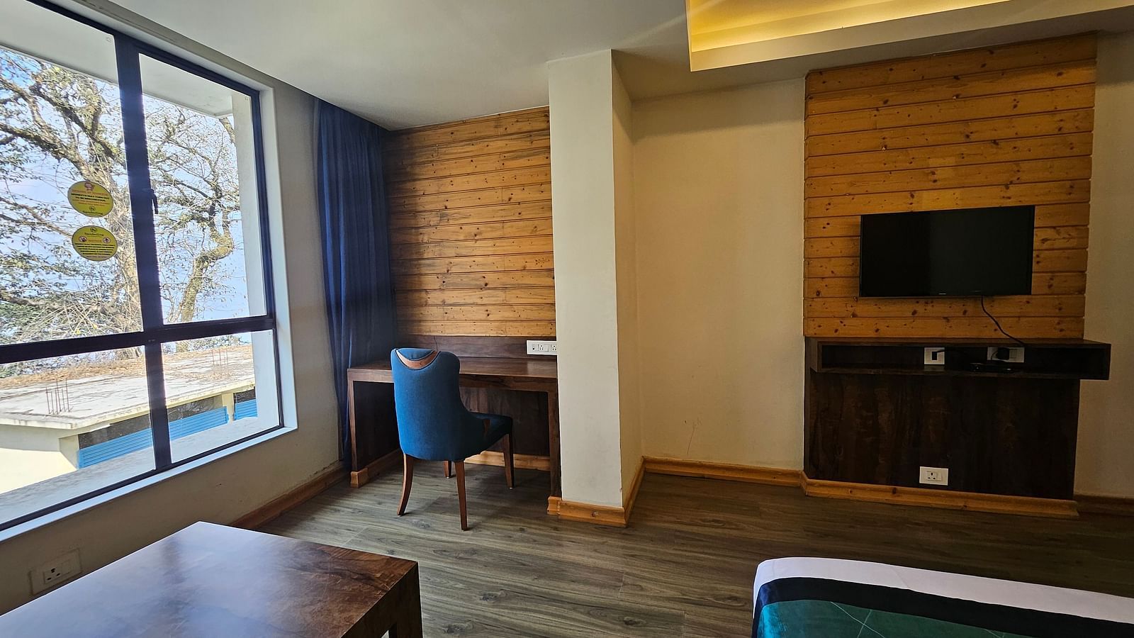 An image of an executive premium room with a flat screen TV, work desk, chair and an expansive window overlooking the view - Yashshree Sanderling, Darjeeling