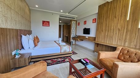 An wider shot of a room at Bamboo Saa Mulberry Resort, with a bed, seating area, a television, and a decorative rug.