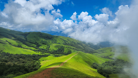 An overview of Kudremukh in Chikmagalur, one of the best places to visit near Bangalore, with greenery all around and fog touching the peak, as seen during day time.