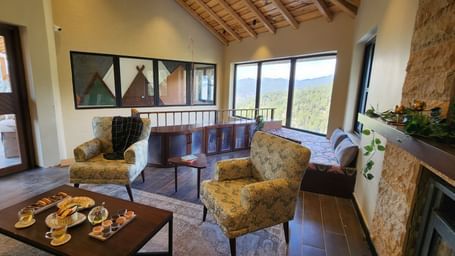 Cosy lounge with armchairs, coffee table, and panoramic window views at The Chamomile Estate.