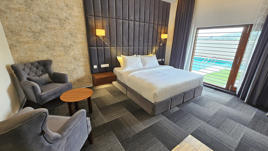 A full-view shot of the Premium Room at Eminence The Corbett with a comfortable double bed and huge windows besides it overlooking the lawn - Rooms in Ramnagar